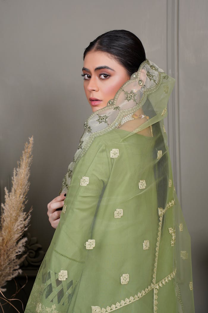 A portrait of a woman in a green embroidered dress, showcasing traditional Pakistani fashion.
